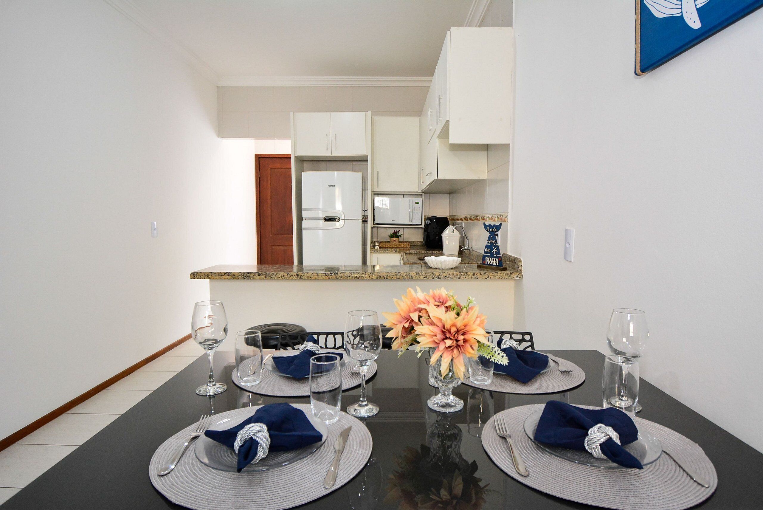 Un comedor con una mesa preparada para cuatro, un refrigerador y una encimera de cocina al fondo.