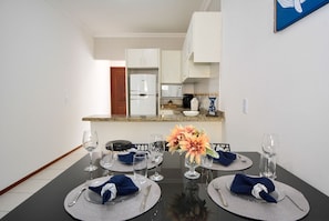 A dining area with a table set for four, a refrigerator, and a kitchen counter in the background. - Refúgio do Mar Centrinho Ingleses-NIN017 (Florianópolis)