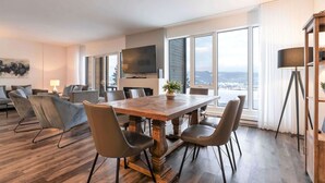 Ein moderner Essbereich mit Holztisch und Stühlen, einem Flachbildfernseher und großen Fenstern mit Blick.