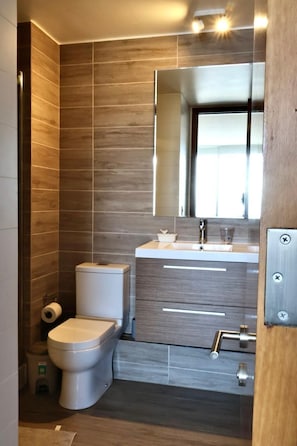 A modern bathroom with a toilet, sink, and mirror. - APARTS SUITES COSTA DE MONTEMAR (Concón)