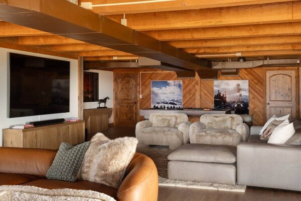 A modern living room with a large flat-screen TV, a pool table, and multiple seating areas with plush sofas. - The Lodge at Four Peaks Ranch (Gallatin County)