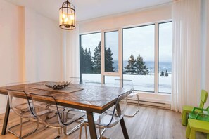 A dining area with a large table, chairs, and a view through large windows. - 109 | Peaceful heaven with beautiful terrace (Baie-Saint-Paul)