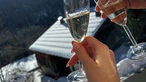 Deux mains tenant des coupes de champagne, avec en arrière-plan un paysage montagneux enneigé et une maison.