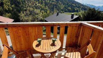 A wooden deck with a round table and two chairs, overlooking a forested mountain range.
