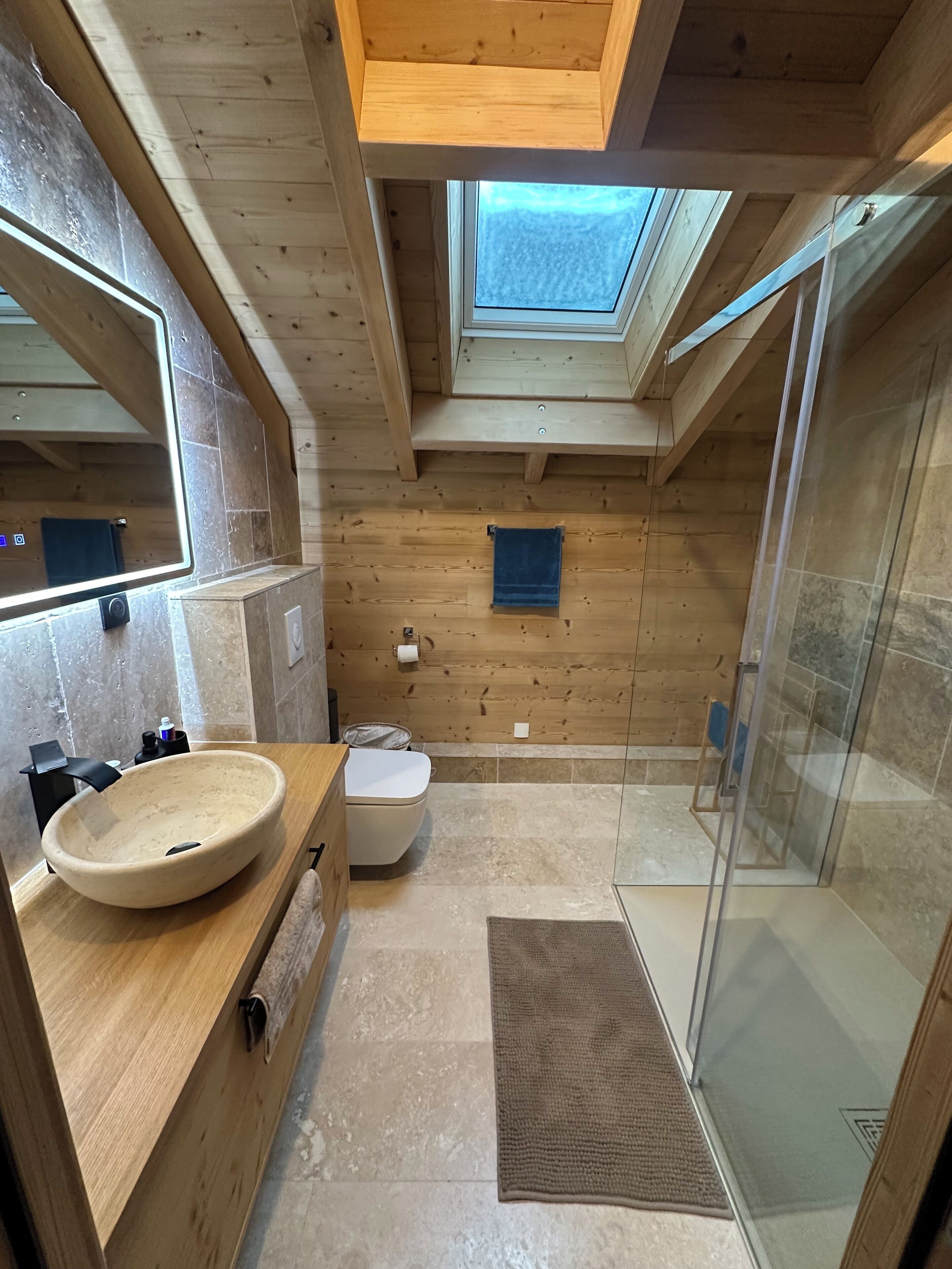 Un baño moderno con tragaluz, paredes de madera, un lavamanos grande y una ducha de vidrio.