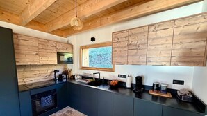 Une cuisine moderne avec des meubles en bois, un four encastré et une fenêtre donnant sur un paysage verdoyant.