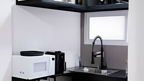 Cocina compacta con fregadero, microondas y estantes para guardar.