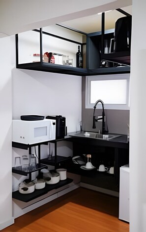 Cozinha compacta com pia, micro-ondas e prateleiras para armazenamento.