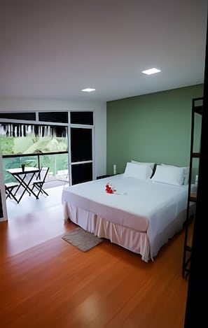 Quarto moderno com uma cama grande, varanda com mobiliário exterior e vista para vegetação.