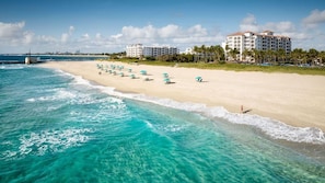 Una playa con aguas turquesas cristalinas, una hilera de sombrillas y un hotel al fondo.