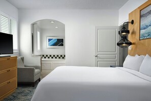 Une chambre d’hôtel comprenant un lit, une télévision, un bureau, une chaise, une lampe fixée au mur et un tableau.