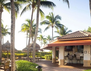 Un resort con mesas al aire libre, palmeras y una zona de bar.