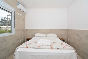 A hotel room with a bed, a window, and an air conditioning unit. - Apartamento Praia dos Ingleses - NIN015 (Florianópolis)