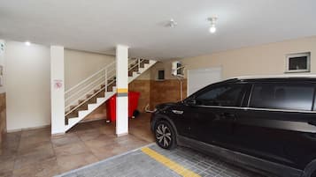 A parking garage with a black SUV, a staircase, and a red trash bin.