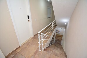 Un escalier avec une rampe en métal, des murs de couleur beige et une porte blanche.