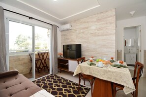 Un coin repas avec une table dressée pour quatre personnes, un téléviseur posé sur un meuble et une porte-fenêtre coulissante donnant sur un balcon extérieur.
