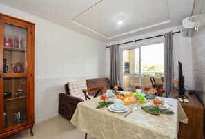 Un coin repas avec une table dressée pour quatre personnes, un buffet en bois avec des portes en verre et un téléviseur posé sur un meuble.