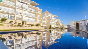 Un hotel moderno con varios balcones, una piscina y un cielo azul despejado.