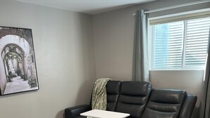 A living room with a black leather sofa, a white coffee table, a patterned rug, and a framed picture on the wall. - Bright & Cozy Basement Suite – Perfect for Work or Adventure (Fort Saskatchewan)