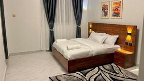 Een netjes ingerichte slaapkamer met een houten bed, een nachtkastje met een lamp, en twee kunstwerken in een lijst aan de muur.