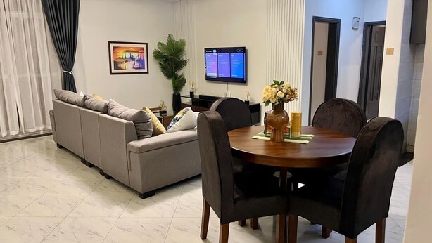 Een moderne woonkamer met een bank, eettafel, stoelen, een televisie en een potplant.