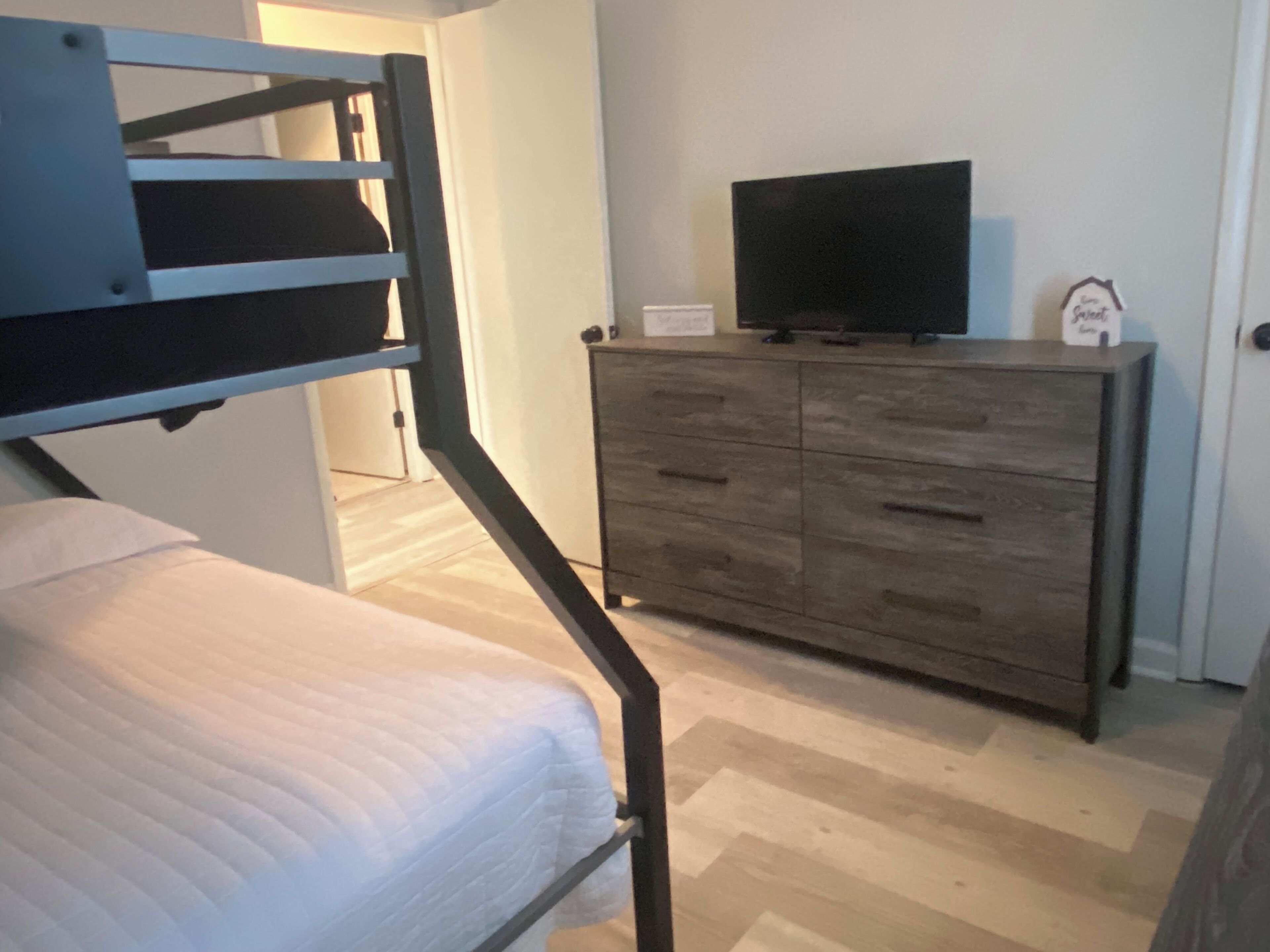 Un lit superposé avec un matelas, une commode en bois sur laquelle est posée une télévision, et une porte avec une pancarte.