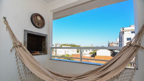 A hammock tied between two windows, a framed picture on the wall, and a view of buildings outside.