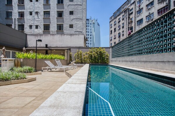 A rooftop pool with lounge chairs and potted plants, surrounded by high-rise buildings. - Apartamento na S c Academia Piscina e Smart Lock (São Paulo)