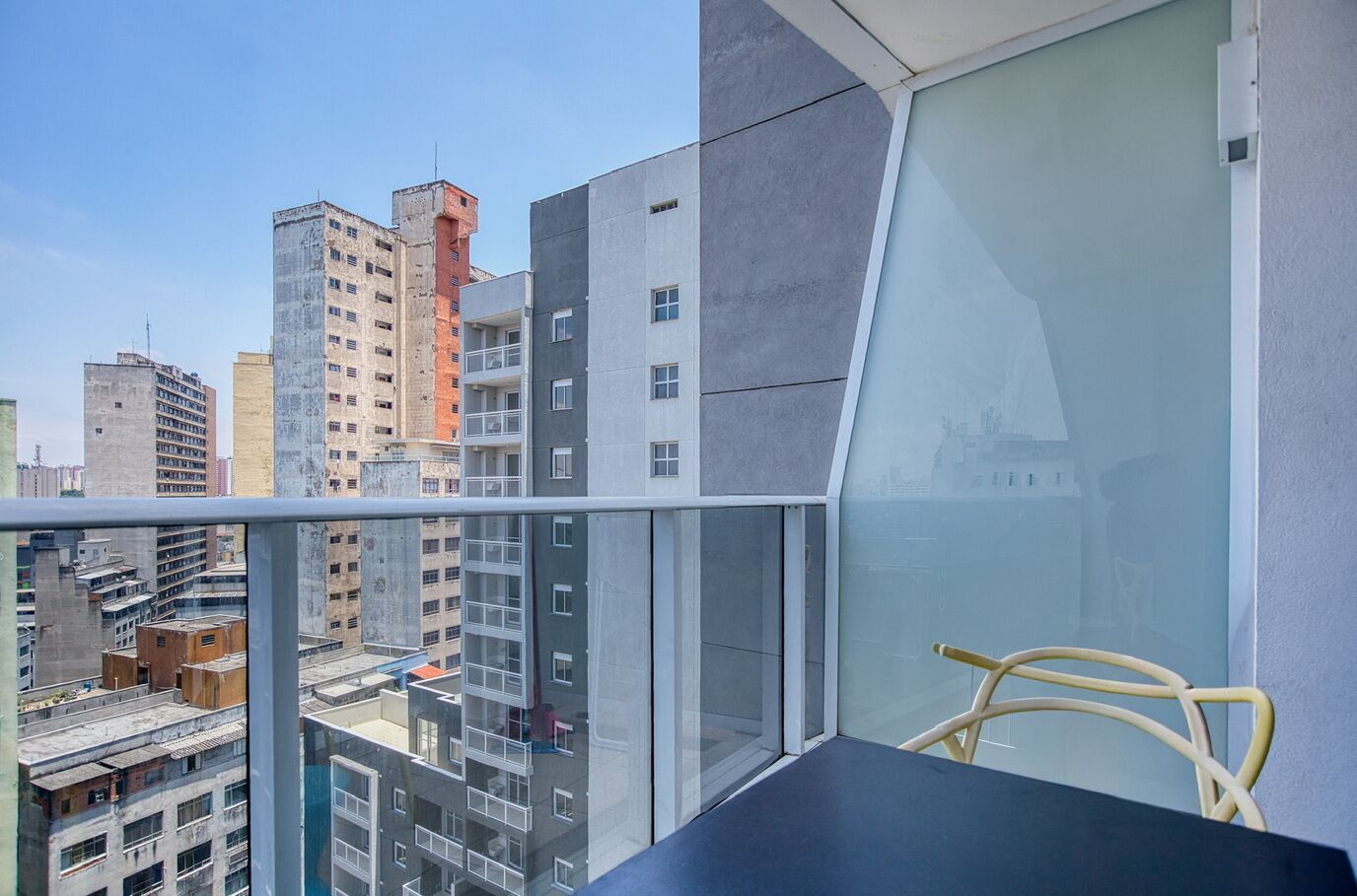 Un balcon donnant sur les bâtiments environnants, avec une chaise et une table.