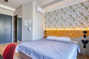 A hotel room with a bed, a red chair, an air conditioning unit, a phone, and a wall with a cityscape pattern. - Apartamento na S c Academia Piscina e Smart Lock (São Paulo)