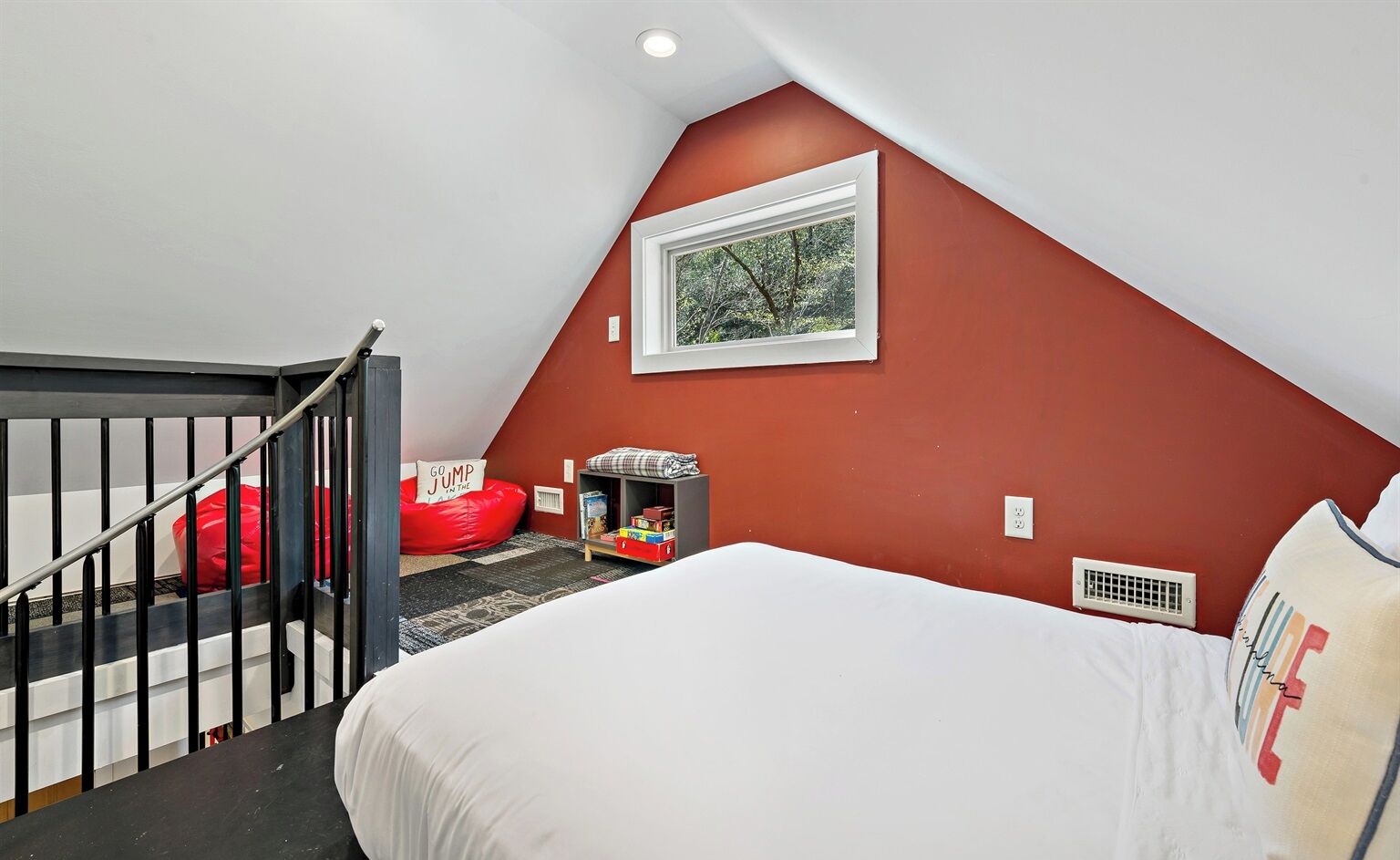 Un dormitorio con techo inclinado, una cama, pared roja, una ventana con vistas y una escalera.
