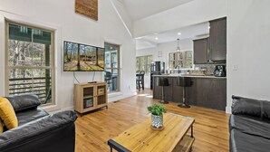 Amplia sala de estar con una mesa de centro de madera, sofás de cuero negro y una cocina con armarios oscuros y una zona de bar.