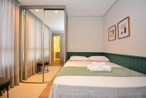 A hotel room with a bed, a chair, a desk, a mirror, and a door leading to another room. - Gaivotas Golden Luxo a 200m praia-NIN012 (Florianópolis)
