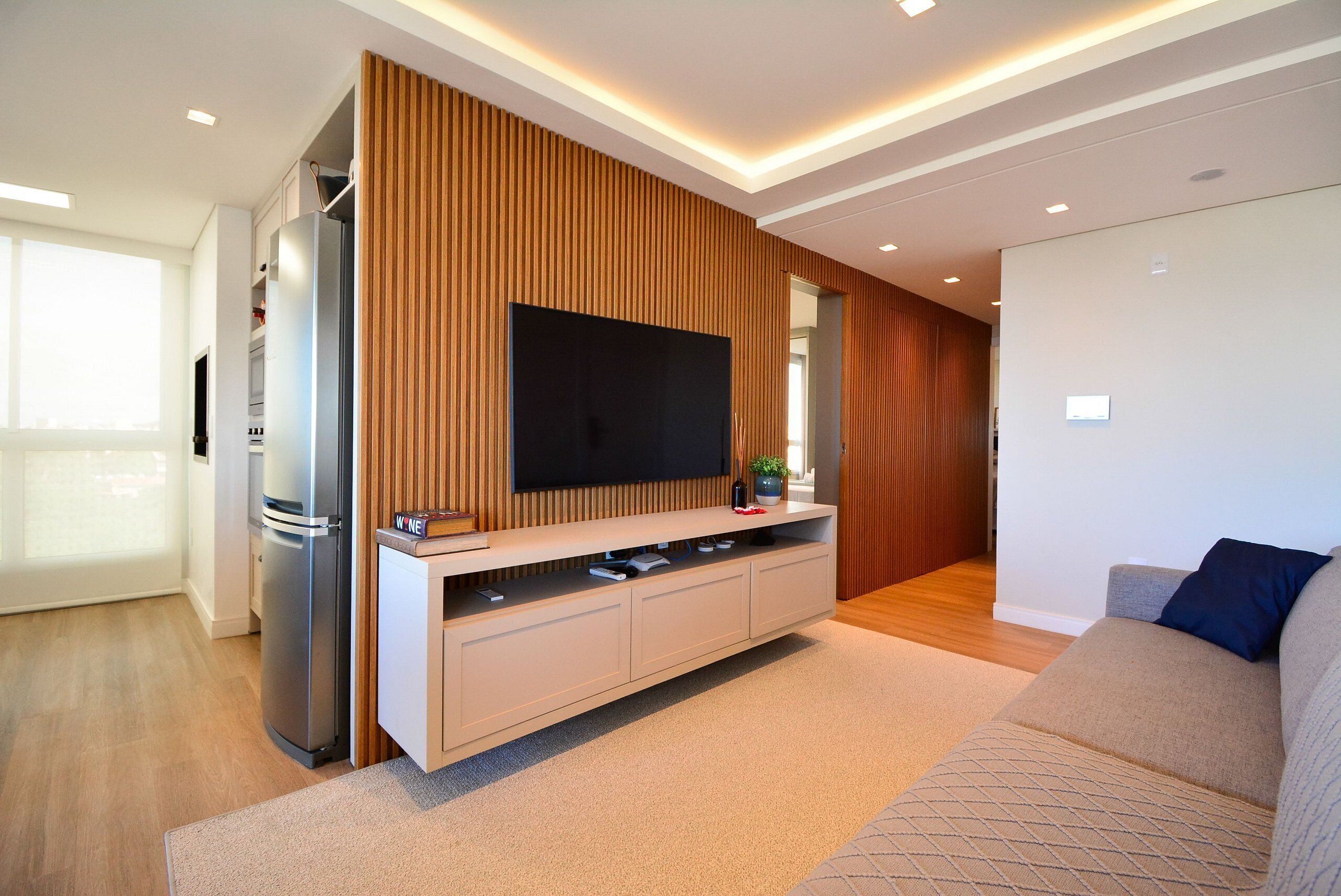 A modern living room with a flat-screen TV, built-in entertainment unit, and a large window.