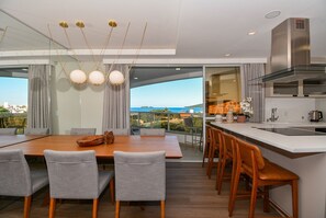 A modern kitchen with a large island, a dining area with a table and chairs, and a view of the ocean. - Gaivotas Golden Luxo a 200m praia-NIN012 (Florianópolis)