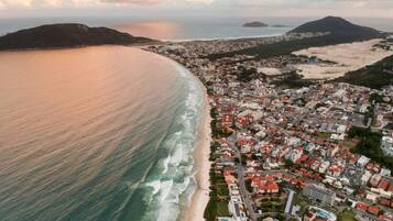 Vista aérea de uma vila costeira com praia, edifícios residenciais e montanhas ao fundo.