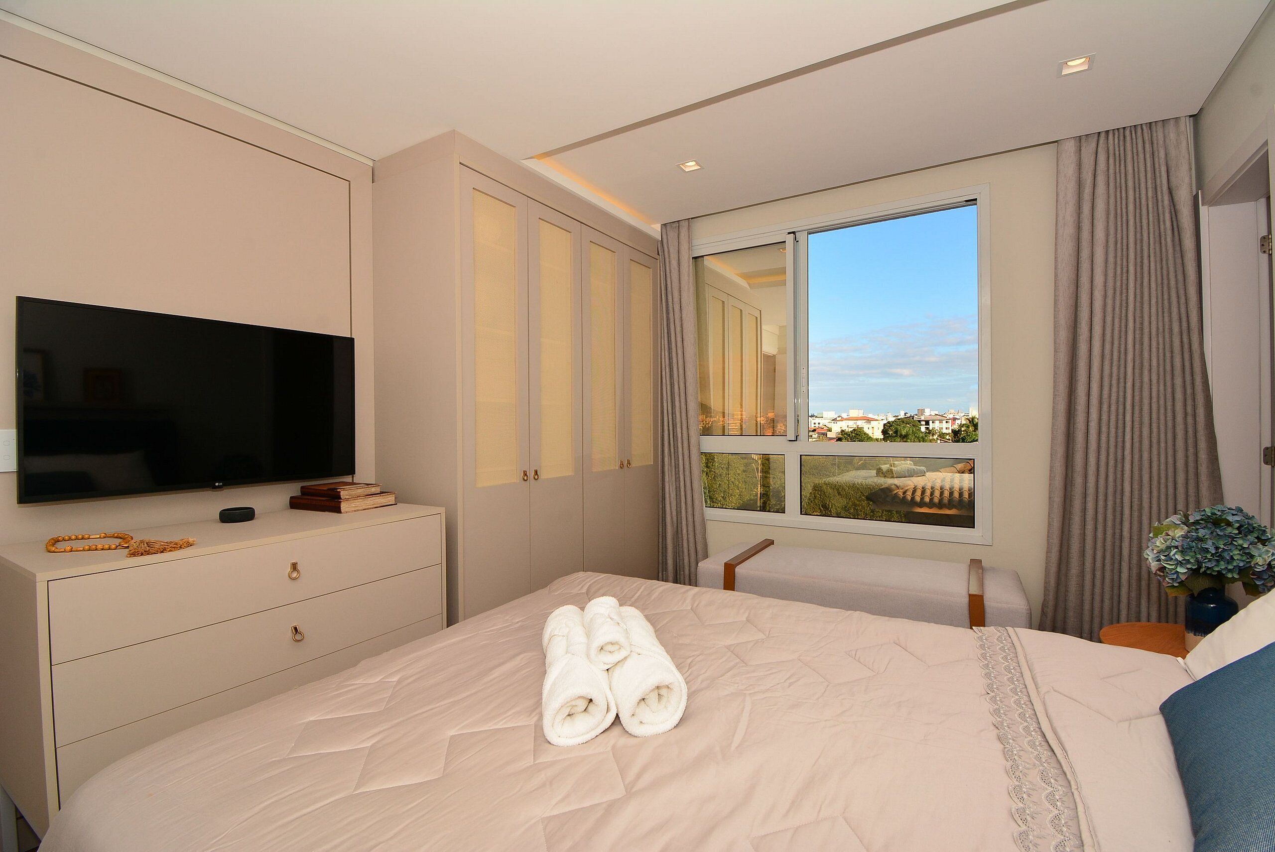 A hotel room with a bed, a TV, a dresser, and a window with a city view.
