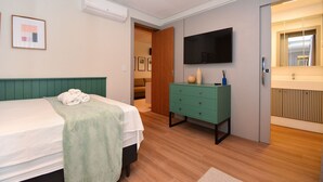 Une chambre d’hôtel avec un lit, une commode verte, une télévision et une salle de bain avec un miroir.