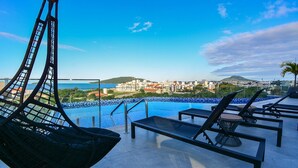 Un espace piscine aménagé sur le toit, avec des chaises longues et un fauteuil suspendu offrant une vue sur le paysage urbain.