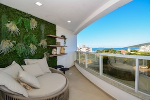 A balcony with a green wall, wicker sofa, and a view of the sea. - Gaivotas Golden Luxo a 200m praia-NIN012 (Florianópolis)