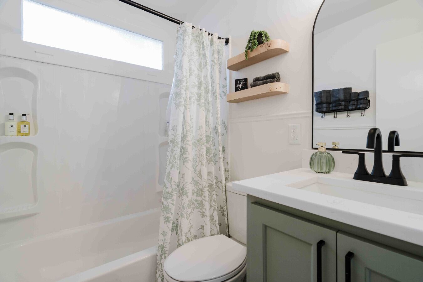 A modern bathroom with a shower, toilet, and vanity. There are shelves with toiletries and a mirror above the sink.