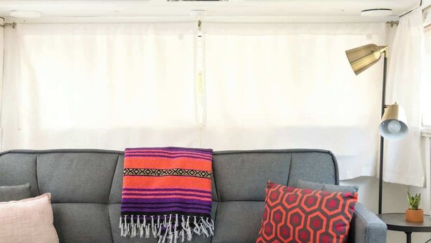 A grey sofa with a colorful blanket and patterned pillows, a wooden coffee table with a plant, and a patterned rug. - Rhonda the Rambler- Glamp w/Pets (Austin)