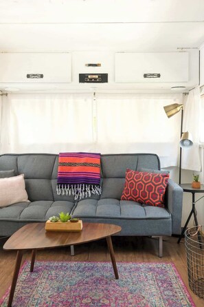 A grey sofa with a colorful blanket and patterned pillows, a wooden coffee table with a plant, and a patterned rug. - Rhonda the Rambler- Glamp w/Pets (Austin)