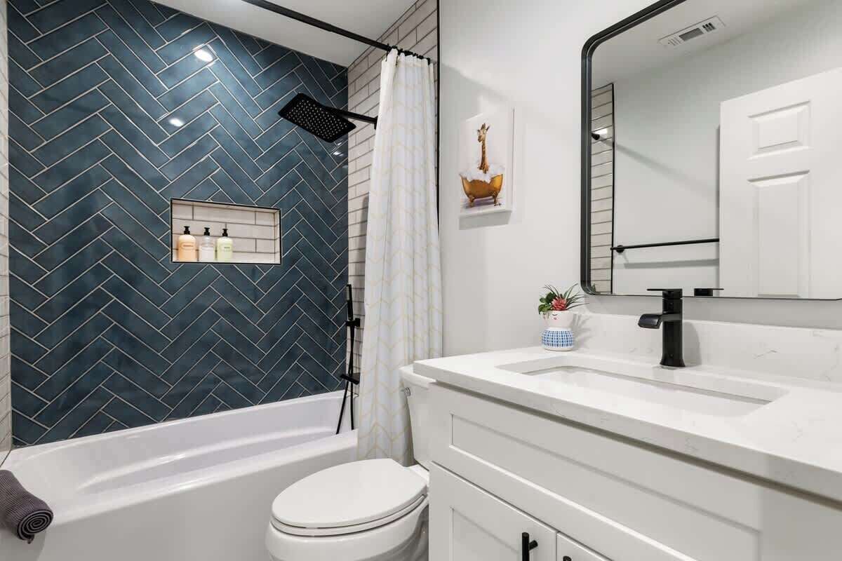 A modern bathroom with a herringbone tile backsplash, a white vanity with a black faucet, and a shower with a gold decorative item.