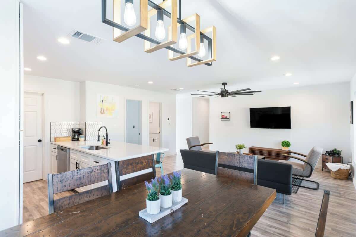 A modern kitchen with a central island, a dining area with a wooden table and chairs, and a living space with a sofa and a TV.