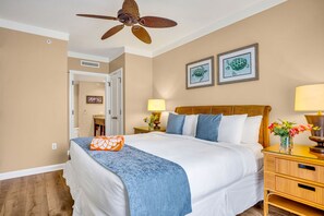 Ein Hotelzimmer mit einem Bett, einem Deckenventilator, zwei gerahmten Bildern an der Wand und einem Nachttisch mit einer Lampe.