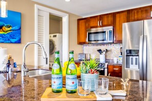Eine Küche mit einer Granit-Arbeitsplatte, zwei Pellegrino-Wasserflaschen, einem Topf mit Pflanze und einem Edelstahl-Kühlschrank.