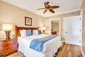 Habitación de hotel con cama, dos lámparas de noche, una mesita de madera, un ventilador de techo, una puerta y un espejo.