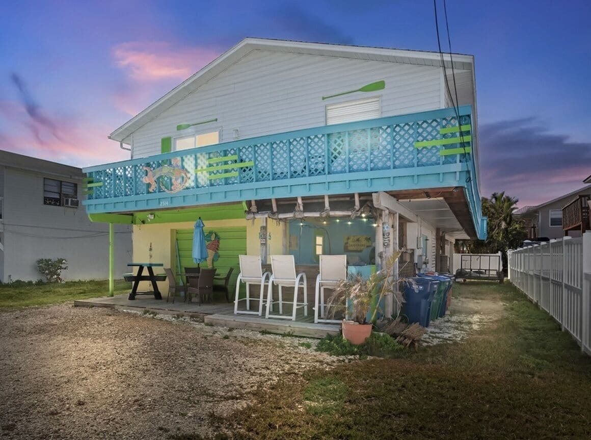 Ein zweistöckiges Haus mit einer Veranda, Sitzgelegenheiten im Freien und einem kleinen Garten.