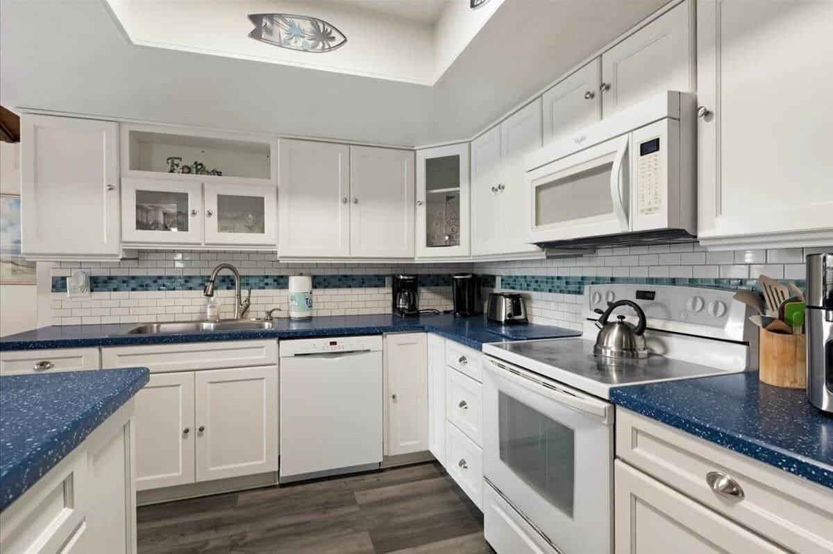A modern kitchen with white cabinetry, a blue countertop, a microwave, a kettle, and a coffee maker.